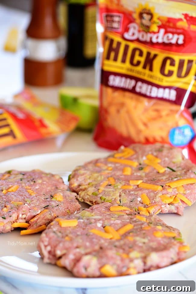 Ingredients for Apple Cheddar Pork Burgers mixed: ground pork, grated apples, fresh rosemary, and sharp cheddar cheese, ready to be formed into patties.