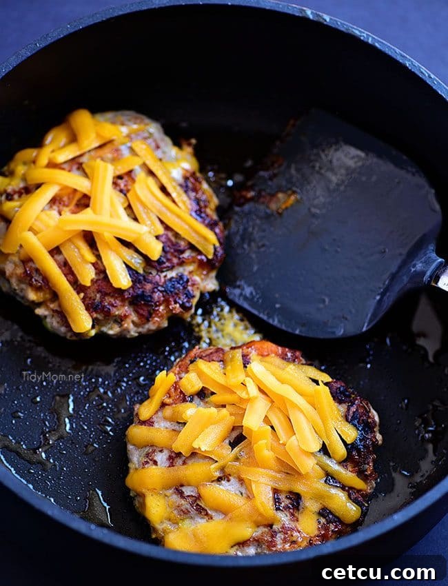 Apple Cheddar Pork Burgers sizzling in a skillet, cooking to golden perfection, ready for the final cheese melt and serving.