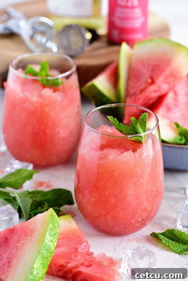 Several stemless wine glasses filled with fresh Watermelon and Grapefruit Wine Slush, garnished with mint, sitting on a light-colored surface. The focus is on the inviting texture and vibrant color.