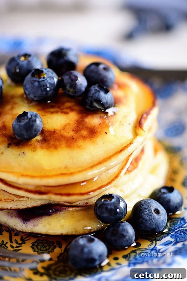 A glorious stack of the Best Homemade Blueberry Pancakes, perfectly golden and generously dotted with blueberries, presented enticingly on a white plate, inviting indulgence.
