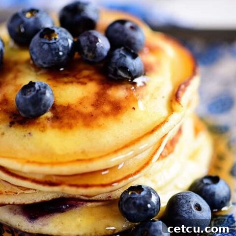 A stack of the Best Homemade Blueberry Pancakes, perfectly golden and bursting with blueberries, ready to be served. Print the full recipe now!