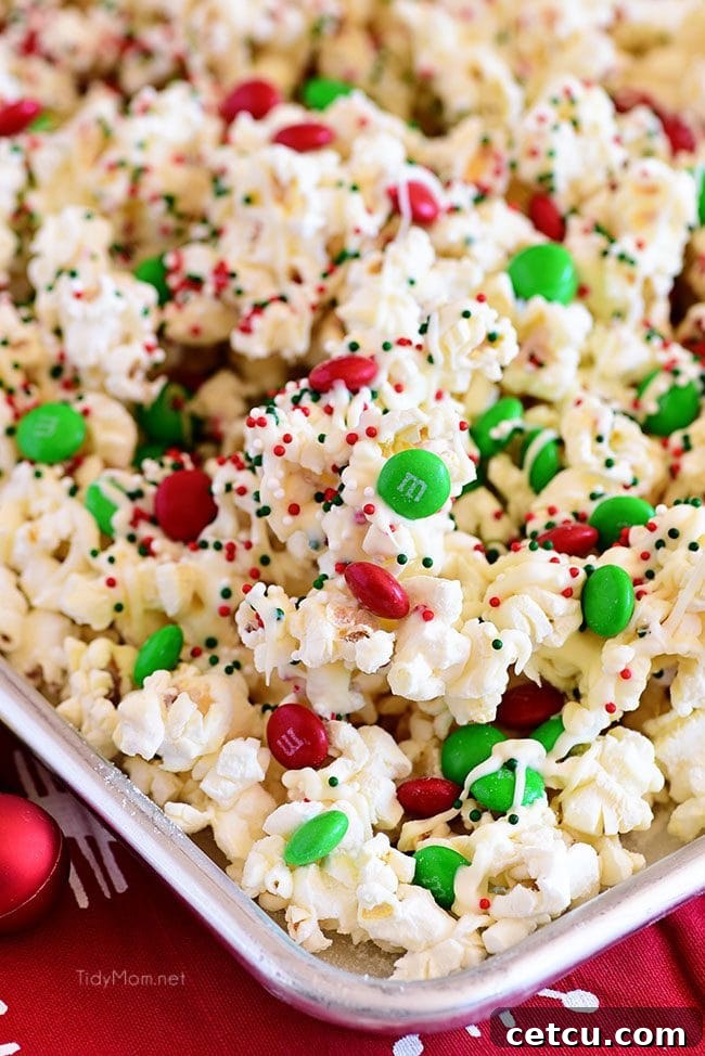 Close-up shot of Santa Munch Christmas Popcorn spread on a baking sheet, with melted white chocolate and colorful sprinkles, ready to cool and harden.