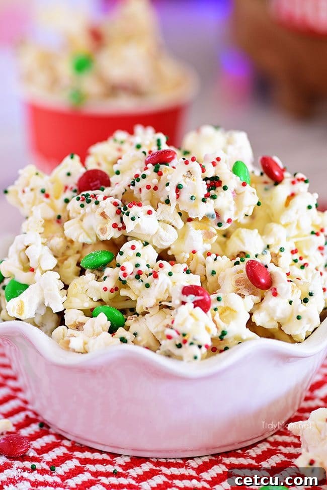 A close-up of Christmas Popcorn in a white bowl, highlighting the colorful candies, sprinkles, and white chocolate coating.