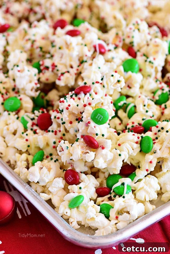 Close-up shot of Santa Munch Christmas Popcorn spread on a baking sheet, with melted white chocolate and colorful sprinkles, ready to cool and harden.