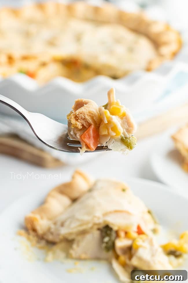 A fork holding a bite of creamy chicken pot pie, with the full pie blurred in the background, inviting a taste.