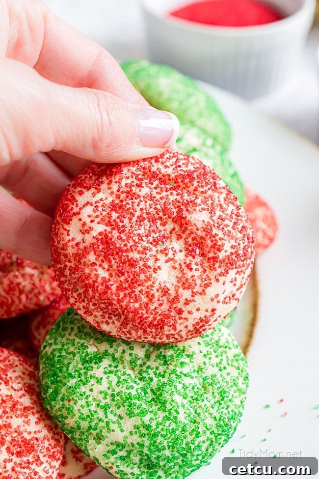 A woman's hand delicately holding a single, vibrant red Christmas drop sugar cookie, showcasing its perfect round shape and festive sparkle.