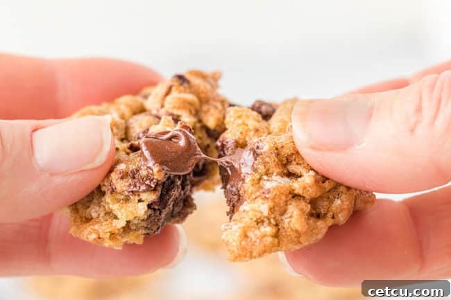 a freshly baked Ranger Cookie broken open, revealing its chewy interior with visible oats, rice cereal, and melted chocolate chips.