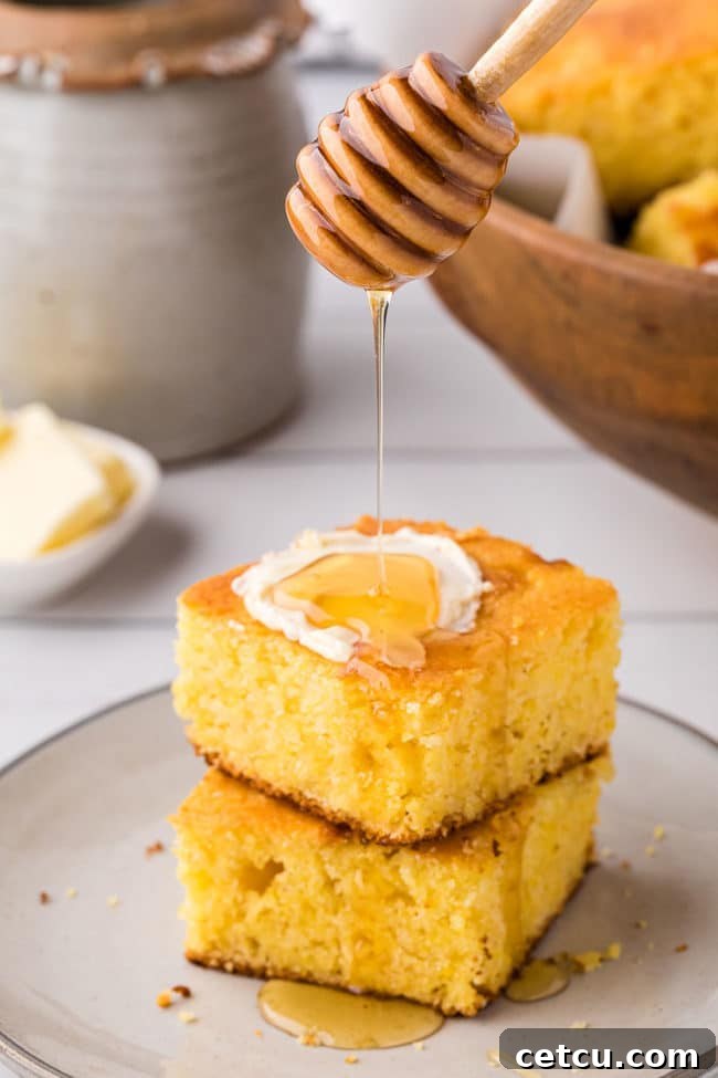 Two servings of golden, moist cornbread, stacked and generously drizzled with honey, highlighting the perfect texture.