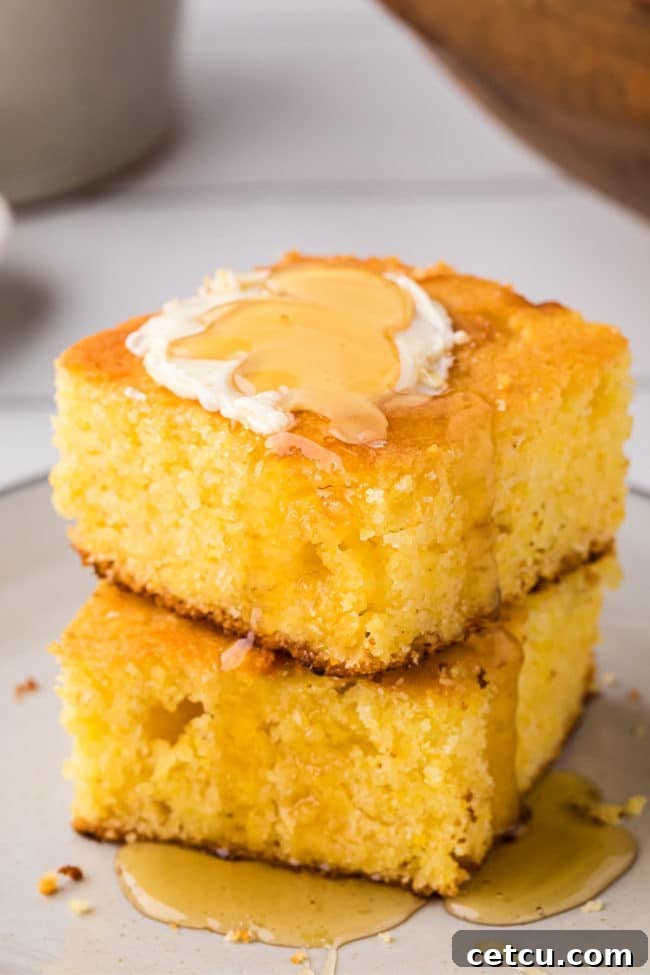 Two pieces of golden cornbread, stacked and topped with a pat of melting butter and a drizzle of sweet honey.