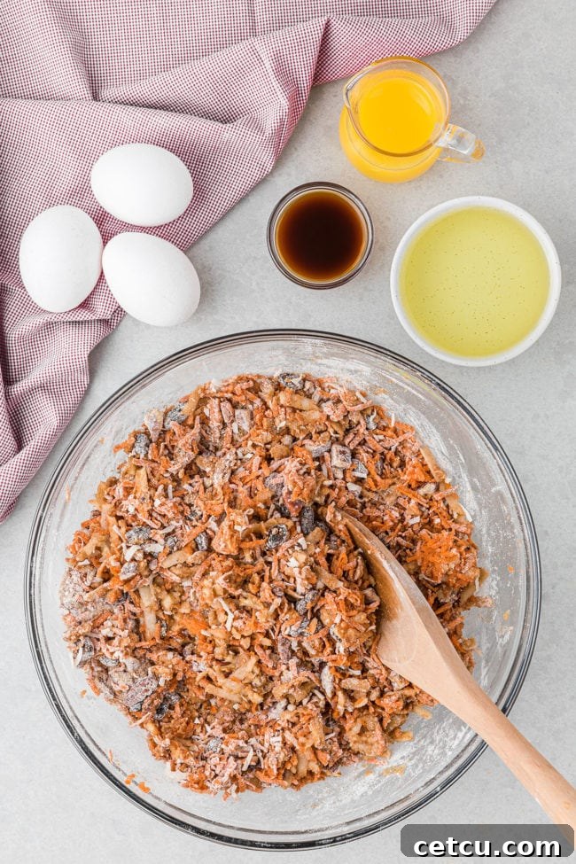 morning glory muffin batter with grated carrots in a glass bowl with a wooden spoon