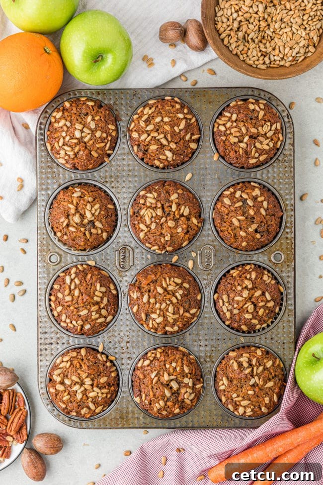 muffins in a pan, with carrots, apples, orange and nuts on the counter around the pan