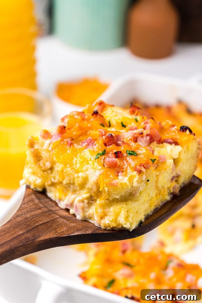 A serving of egg casserole being lifted from the baking dish with a wooden spatula, showcasing its fluffy texture.