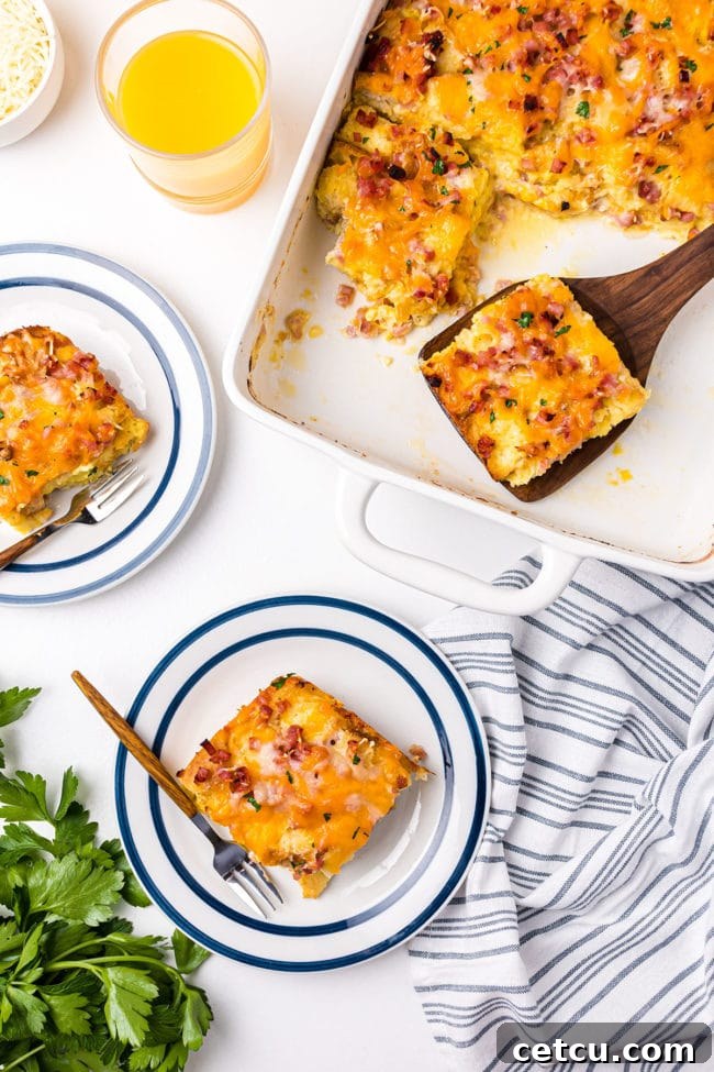 Individual servings of English Muffin Breakfast Casserole on plates, with the remaining casserole in a white baking dish and a wooden spatula nearby.