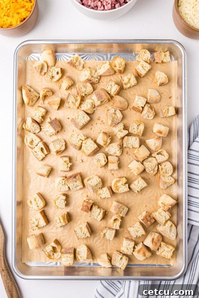 English muffin pieces spread on a baking sheet, lightly toasted, ready for the breakfast casserole assembly.