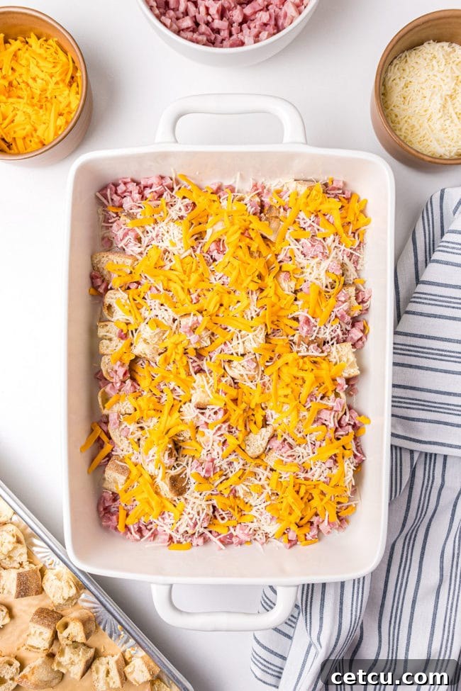 A casserole dish with the first layer of ham and cheese, ready for more ingredients in the English Muffin Breakfast Casserole.