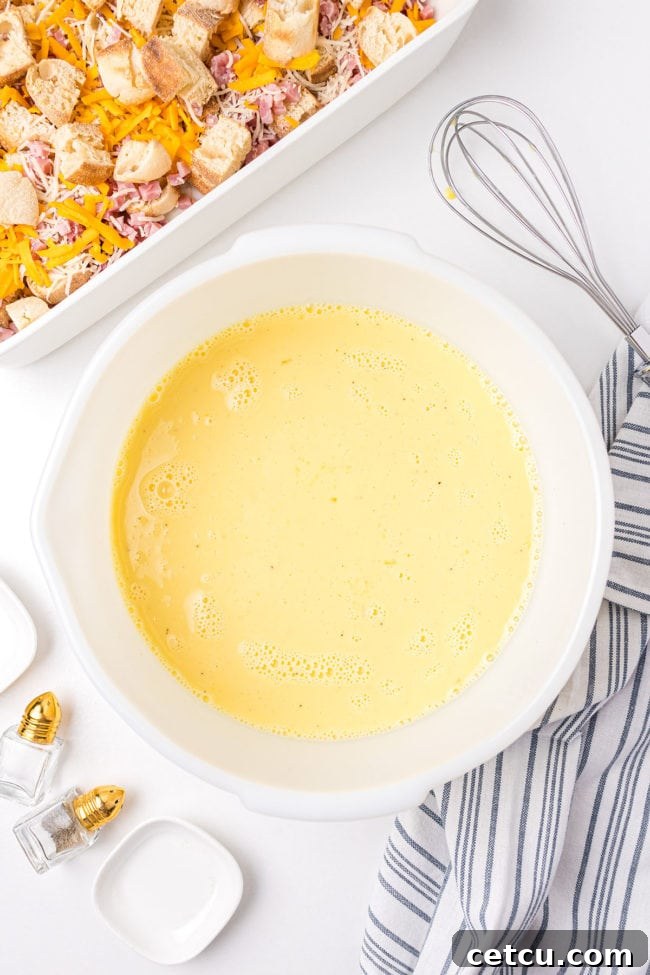 A large bowl containing whisked eggs, half and half, and seasonings, forming the liquid base for the breakfast casserole.