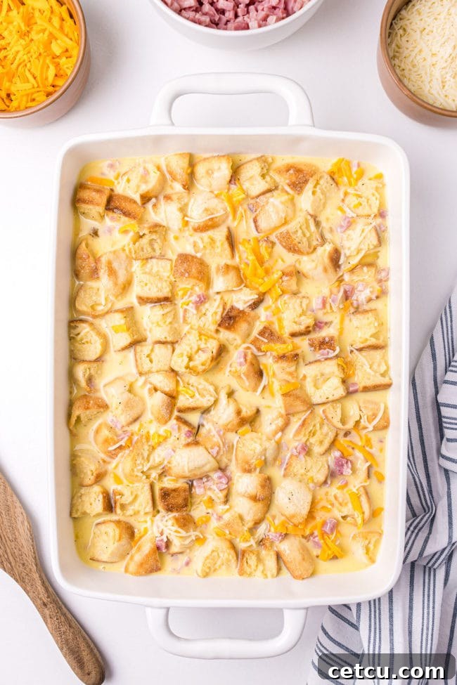 English muffin pieces soaking in the egg mixture within a casserole dish, absorbing the rich liquid for an overnight breakfast bake.
