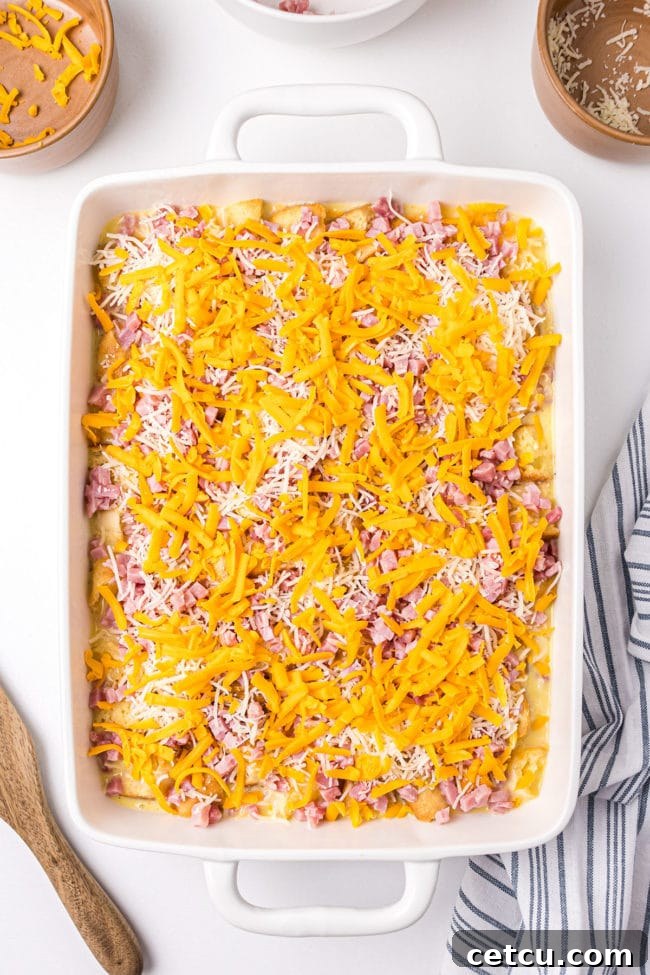 An assembled English Muffin Breakfast Casserole, covered with plastic wrap, ready to be refrigerated overnight before baking.