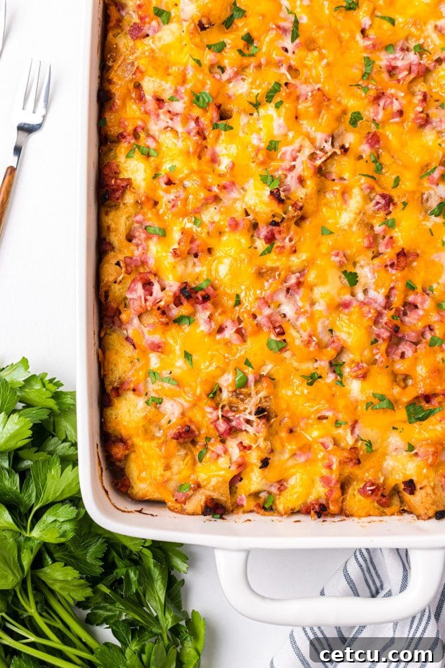 A freshly baked English Muffin Breakfast Casserole, golden brown and bubbly, garnished with fresh parsley on a wooden table.