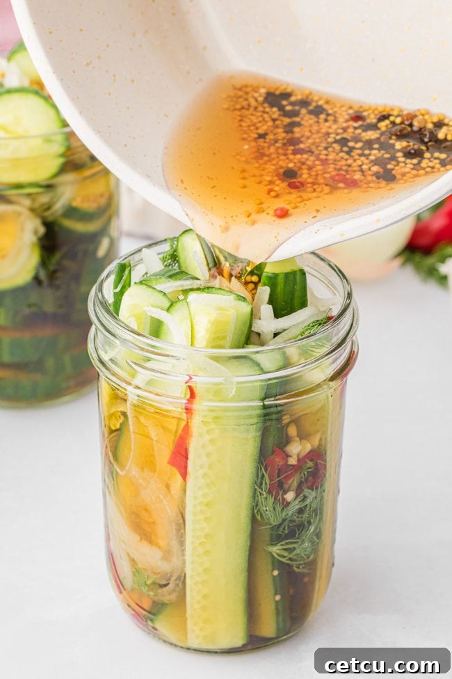 A steady stream of cooled pickling brine being poured over tightly packed cucumber spears and fresh dill in a glass jar, ensuring full submersion for optimal flavor.