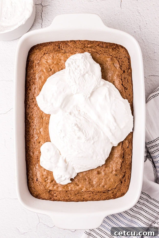 Step 8: Spreading the marshmallow creme evenly over the warm cake after it has softened, creating a smooth, gooey layer.