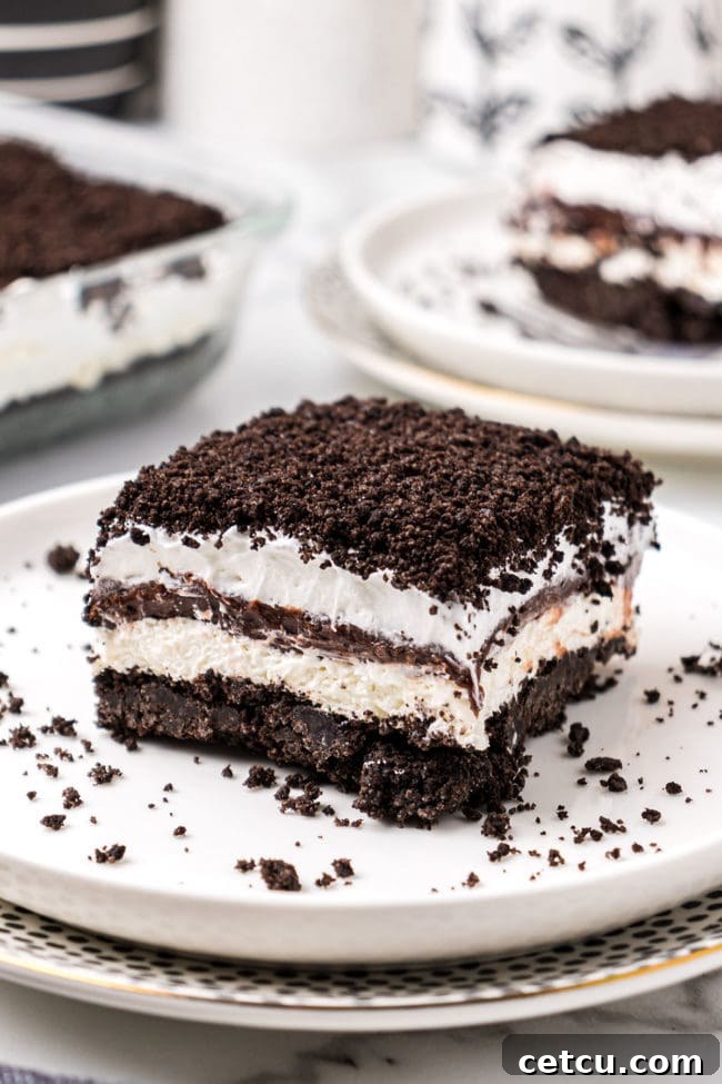 A slice of No-Bake Oreo Delight, also known as chocolate lasagna, on a white plate, showcasing its distinct layers of Oreo crust, cream cheese, chocolate pudding, and whipped topping.