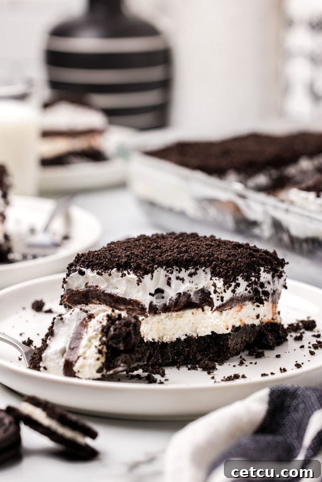 A delicious slice of layered chocolate lush dessert on a white plate, with a fork taking a bite, showing the rich internal textures.