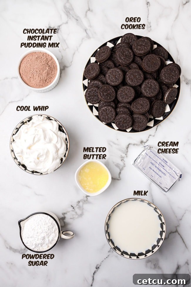 All the fresh ingredients for No-Bake Oreo Delight laid out on a kitchen counter, including a package of Oreos, butter, cream cheese, powdered sugar, Cool Whip, instant chocolate pudding mix, and milk.