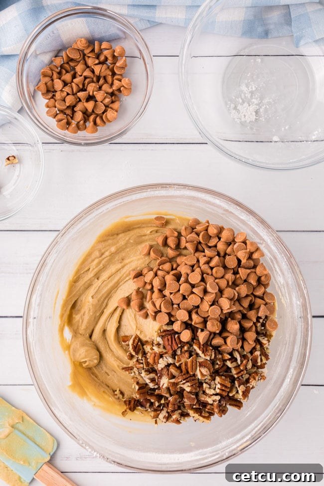 Butterscotch blondie batter with visible butterscotch chips and pecans being mixed in a clear glass bowl, showcasing the rich texture.