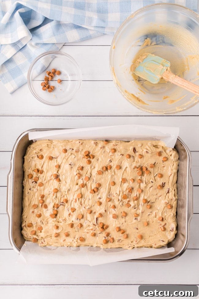Butterscotch blondie batter evenly spread into a 9x13 inch metal baking pan, prepared for the oven.