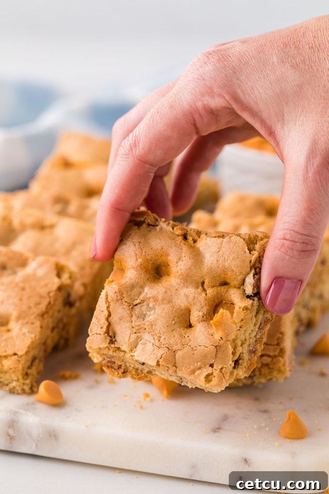 A woman's hand gracefully holding a single butterscotch blondie, highlighting its rich color and inviting texture.