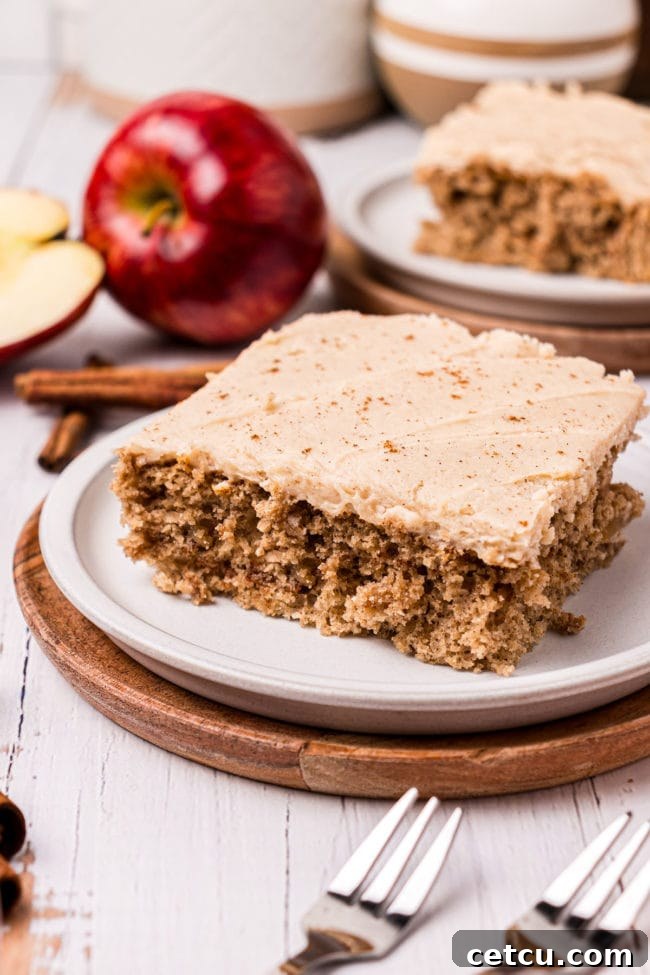 A serving of apple cake on a plate. Red apples in the background.