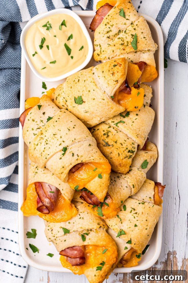 Baked Ham and Cheese Crescent Roll Sandwiches on a white serving tray with a blue striped towel.