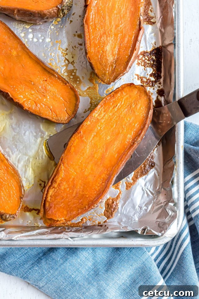 halved sweet potatoes on a baking sheet with a spatula