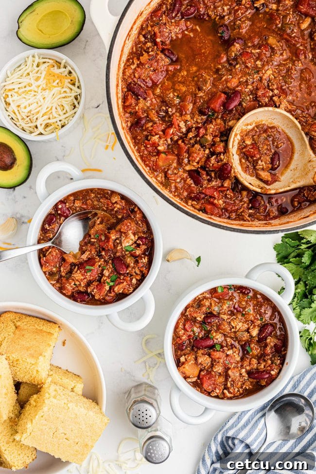 Two white bowls filled with hearty leftover turkey chili, garnished with fresh herbs and a large pot of chili in the background, with cornbread on the side.