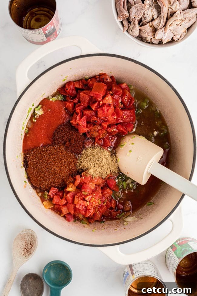 Adding seasonings, fire-roasted tomatoes, and tomato sauce to a pot of sautéed vegetables for leftover turkey chili.