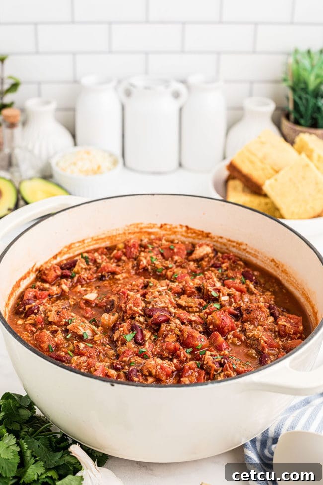 A white Dutch oven filled with simmering, rich turkey chili, showcasing its hearty texture.