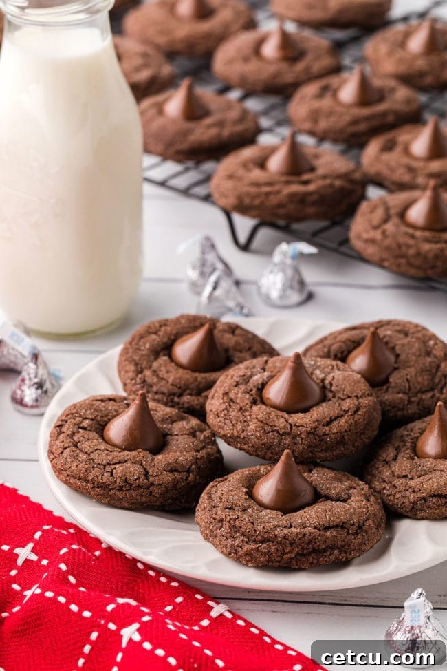 A plate of freshly baked Double Chocolate Kiss Cookies next to a cooling rack and a bottle of milk, ready to be enjoyed.