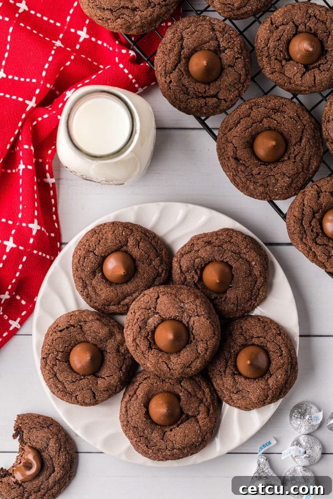 A festive display of Double Chocolate Kiss Cookies arranged on a white plate, accompanied by a glass of milk and a red napkin, evoking a cozy holiday scene.