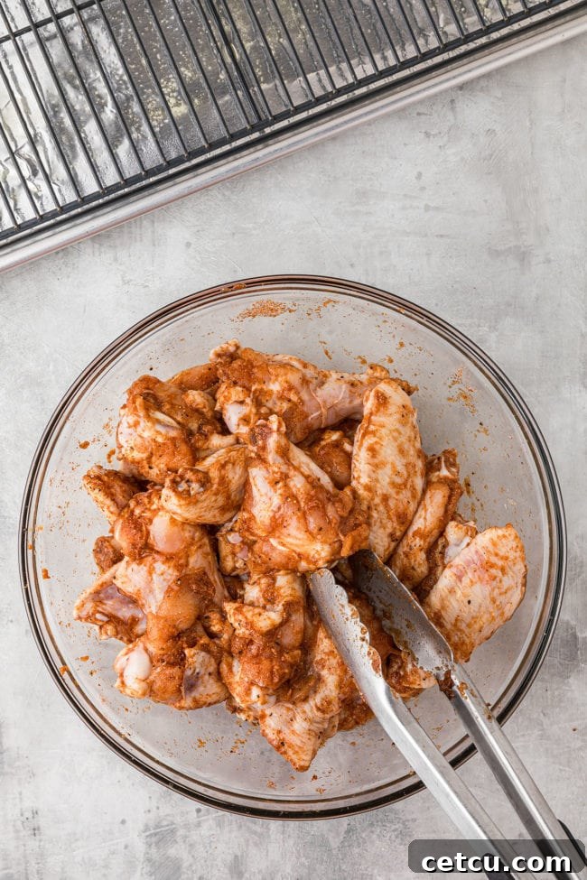 Chicken wings coated in a savory seasoning mix, tossed in a clear glass mixing bowl, showcasing even distribution of spices.