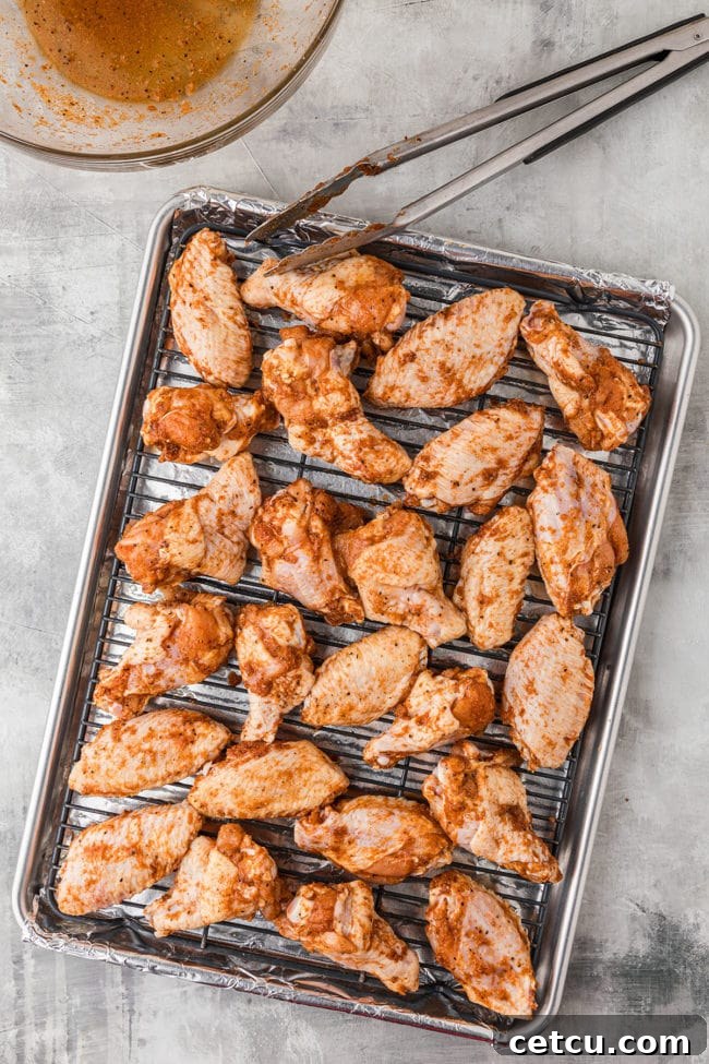 Seasoned chicken wings spread out on a baking sheet lined with foil and a wire rack, ready for the oven.