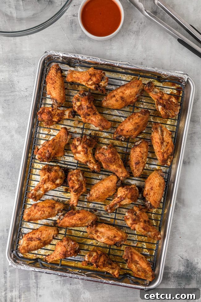 Crispy baked chicken wings with a golden-brown finish resting on a metal baking rack over a foil-lined pan, fresh out of the oven.