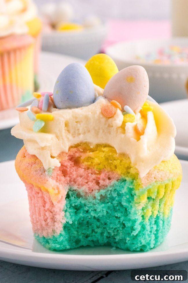 A bite missing from a marble cupcake with Spring colors, showing the pastel swirl inside, decorated with sprinkles and mini chocolate eggs.