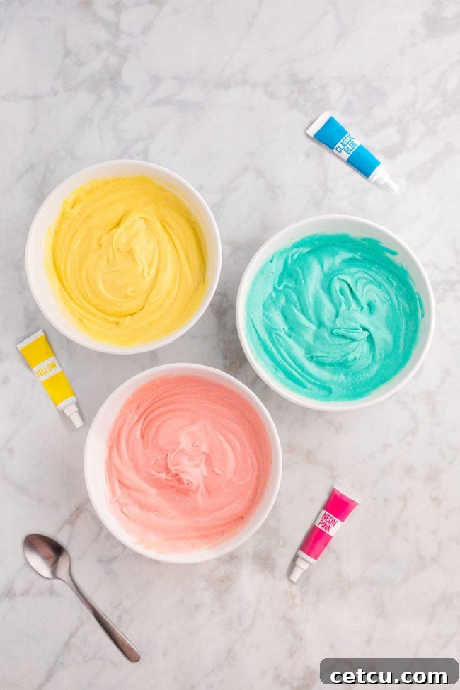 Three separate bowls containing cake batter dyed in pastel yellow, pink, and blue colors, prepared for creating marble Easter cupcakes.