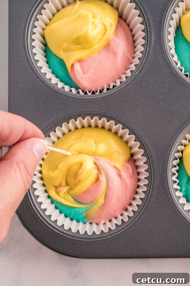 A close-up shot of cupcake liners with three colors of cake batter gently swirled together with a toothpick, creating a marble effect for Easter cupcakes.