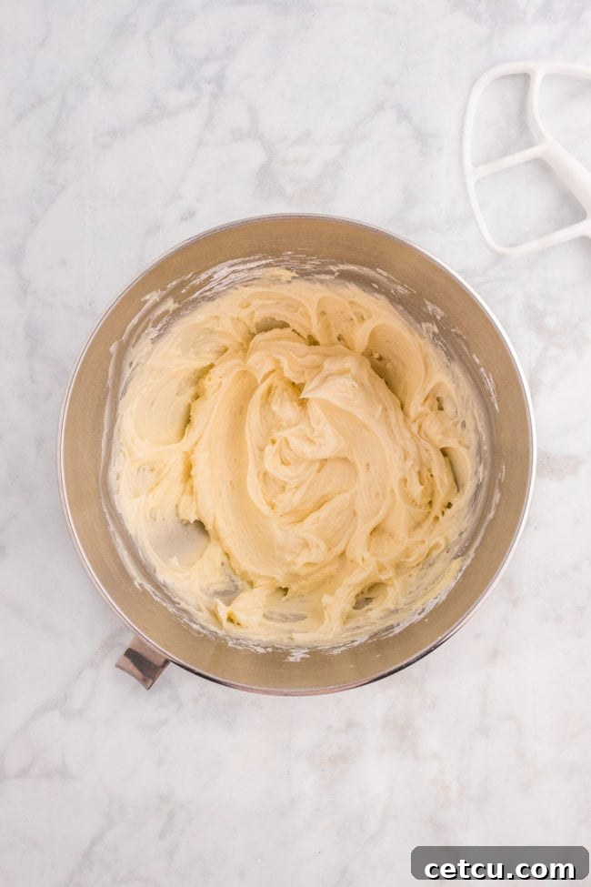 Creamy, white homemade buttercream frosting being beaten in a stand mixer, showing its smooth and fluffy texture.