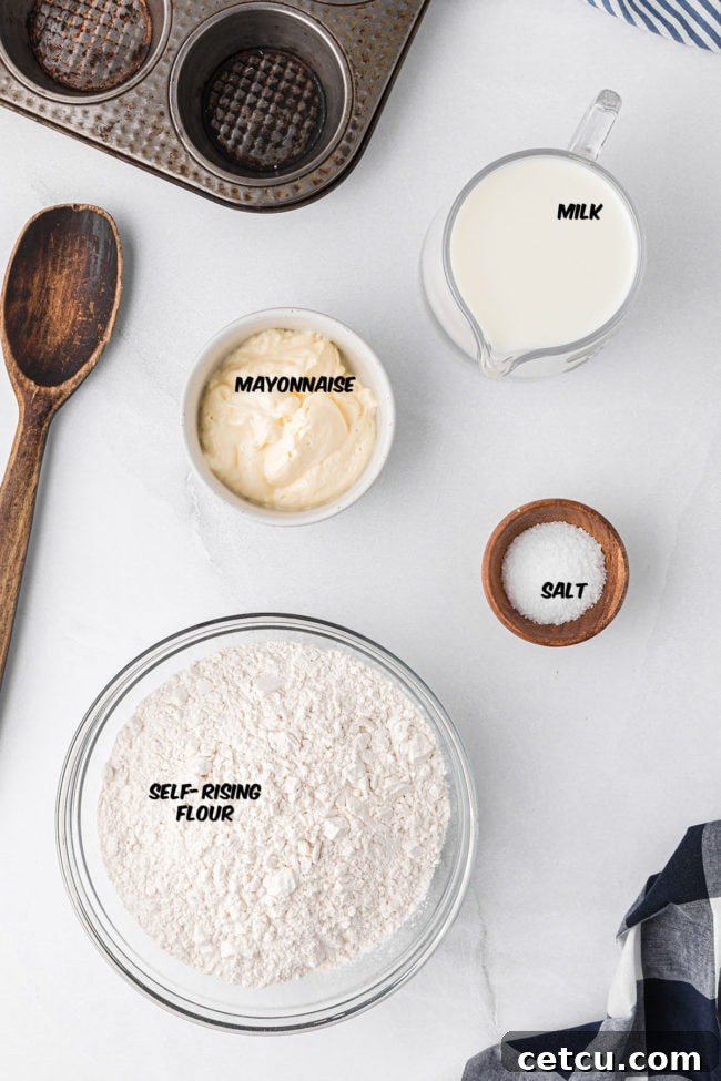 A simple yet elegant flat lay displaying the three key ingredients for making mayonnaise biscuits: a bowl of self-rising flour, a carton of whole milk, and a jar of creamy mayonnaise, along with a measuring spoon.