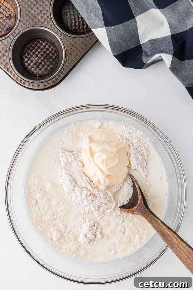 A glass bowl holds the initial ingredients for mayonnaise biscuits, showing the process of mixing the flour, milk, and mayonnaise together.