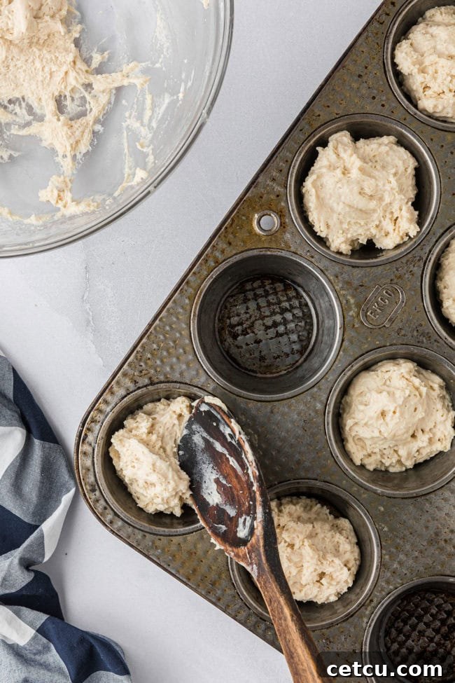 A muffin tin with several cups filled approximately halfway with the wet mayonnaise biscuit dough, prepared for baking.