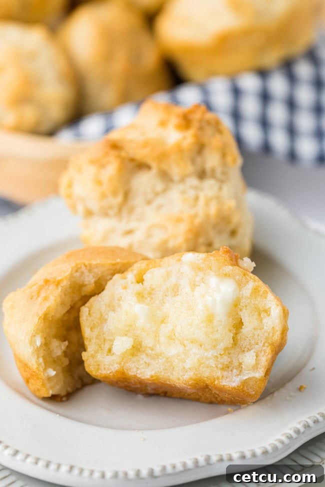A close-up of a warm mayonnaise biscuit, split open and generously spread with melted butter, highlighting its fluffy interior.